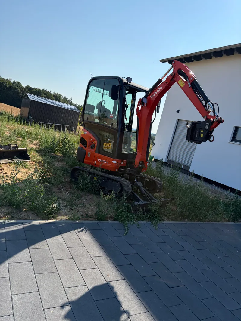 Kubota KX019-4 mit Anbaugerät an einer Hofeinfahrt